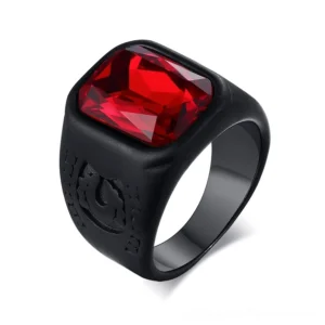 Black stainless steel gothic signet ring with red rectangular glass stone, oblique top view on white background showing embossed emblem details