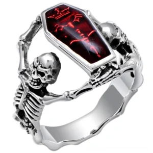 Gothic skeleton coffin ring with red rhinestone, 3/4 front view showing intricate silver skeleton design holding bright red cubic zirconia stone