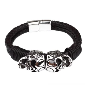 Dual skull gothic bracelet flat lay top-down view, black leather with silver stainless steel charms and magnetic clasp