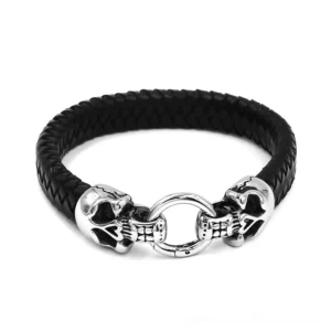 Gothic double skull leather bracelet with stainless steel clasp, flat lay front view showing braided black leather band and dual skull charms