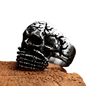 Gothic vintage skull ring for men shown from left side view on wooden surface, displaying intricate cracked skeleton hand design with aged metal finish