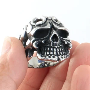 Vintage gothic skull ring held on fingertips, showing detailed carved skull structure and aged silver patina finish
