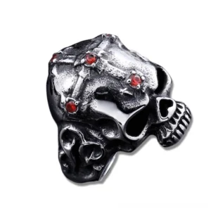 Dark silver skull ring with red stone accents and cross design, front view on white background, twin skull cross pattern with deep crimson gemstone inlay