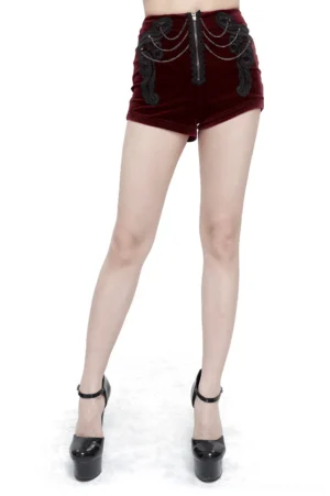 Wine red velvet gothic shorts with front zipper, black lace appliqué, and multi-layer metal chains with gem accents, styled on model with platform heels