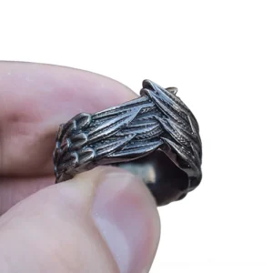 Gothic wing ring held in fingertips, detailed side angle close-up displaying hand-carved feather texture and dark charcoal metal tone