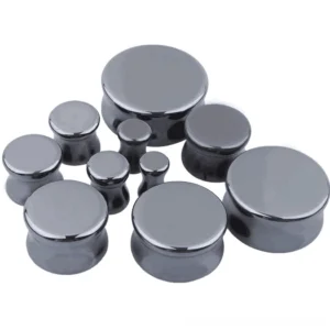 Multiple hematite stone ear expander plugs in different gauges from 6mm to 25mm, overhead flat lay showing size progression and gunmetal gray finish