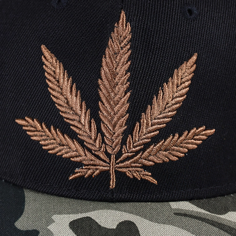 Hand-embroidered brown hemp leaf on black fabric gothic cap close-up with camouflage brim texture
