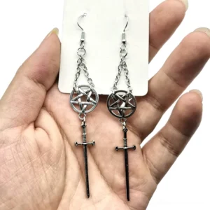 Pentagram and sacred sword gothic dangle earrings in mixed silver and black metal with chain tassels held in hand against jewelry display card