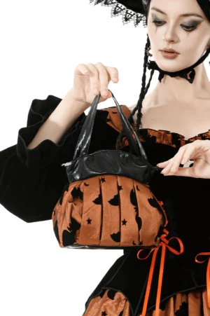 Brown pleated gothic handbag with bat and star print in close-up held by model in witch costume, featuring silver bat zipper charm against white studio background