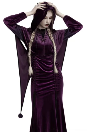 Front view of purple velvet gothic hooded cape with drawstring closure worn by model with blonde braids, showing full-length draping and pointed hem with pompom accents
