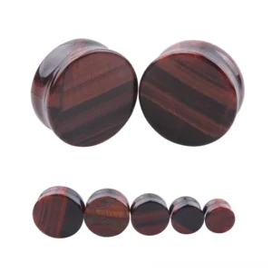 Red tigerite stone ear plugs and flesh tunnels in wine red color with natural striped patterns, displayed at oblique side angle on white studio background, showcasing gothic body jewelry