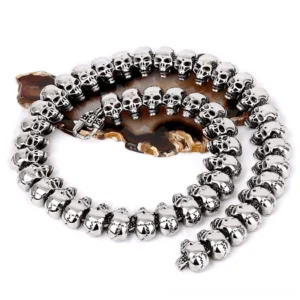 Memento Mori skull link chain necklace in polished 316L stainless steel, displayed flat lay on white background with agate coaster, showing complete necklace structure and ornate clasp