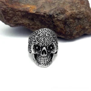 Day of the Dead style skull ring with intricate carved floral patterns and antique silver finish on stone backdrop