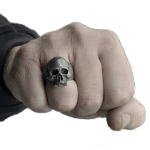 Gothic skull ring worn on male hand middle finger, frontal view against white background