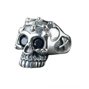 Sterling silver skull ring front view showing detailed skull face with black gemstone eyes, cross-embossed crown, vintage oxidized finish, and polished silver accents on pure white background