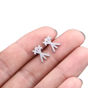 Minimalist silver stick-figure gothic rune earring in human fingers, overhead shot displaying matte silver stainless steel aesthetic