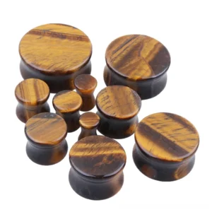 Overhead flat lay collection of yellow tigerite ear flesh tunnels and gauges showing graduated size progression from small to large for alternative gothic style