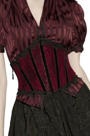 Wine red and black lace gothic corset worn by model, front three-quarter view showing intricate lace panels and black velvet trim detail